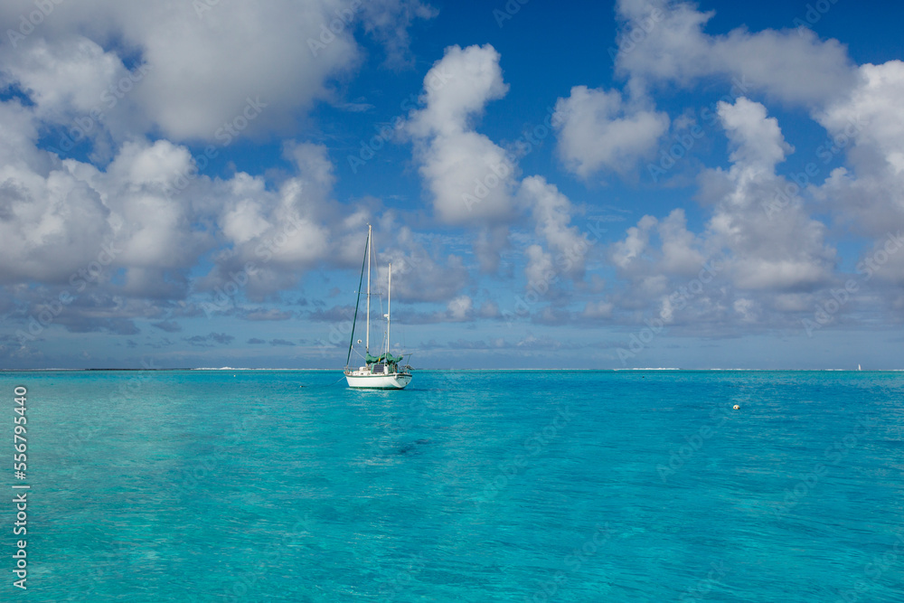 A lone sailboat anchored off shore in the turquoise waters of the South Pacific with puffy, white clouds in a blue sky in the lagoon in Tahaa; Tahaa, French Polynesia A lone sailboat anchored off shore in the turquoise waters of the South Pacific with puffy, white clouds in a blue sky in the lagoon in Tahaa; Tahaa, French Polynesia