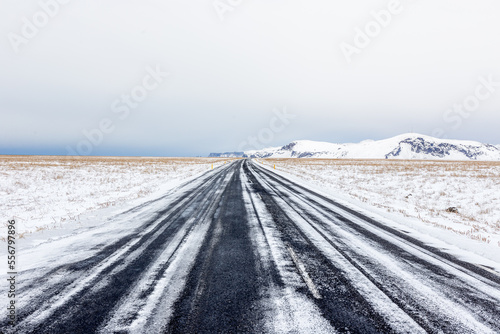 Strada rettilinea ricoperta di neve appena dopo una leggera nevicata con cielo nuvoloso, montagna all'orizzonte