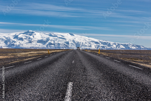 strada rettilinea asfaltata con auto bianca in direzione di una montagna ricoperta di ghiaccio in una giornata serena islanda