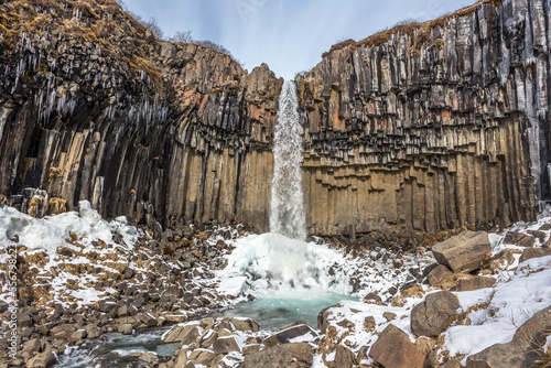 Cascata Svartifoss, torrente che salta da rocce basaltiche, ghiaccio alla base, stalattiti di ghiaccio sulle pareti, sassi sul letto del torrente
