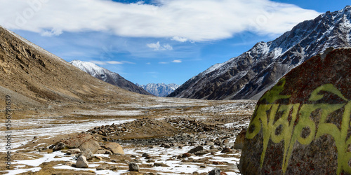 Icy valley with mantra painted on rock and snow capped mountains behind in the foothills of the Himalayas in the Ladakh Region; Jammu and Kashmir, India photo