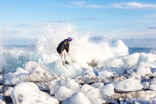 Persona in equilibrio precario sopra un iceberg arenato che sta per essere travolta sa una grande onda con luce calda e cielo azzurro photo