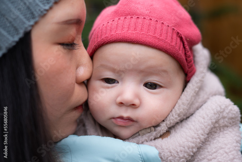 young happy and attractive Asian Chinese woman holding baby girl in her arms in front of Christmas tree walking on Winter street market in mother and daughter love concept