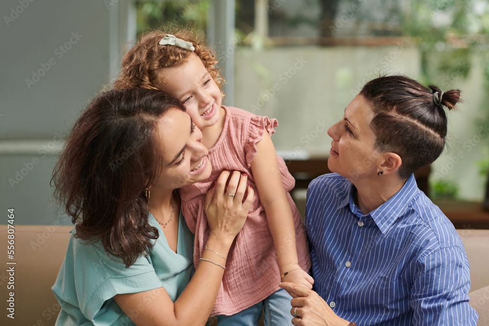 Cheerful mothers hugging their little daughter when resting on sofa at home Cheerful mothers hugging their little daughter when resting on sofa at home