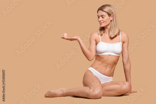 Woman with jar of body cream on beige background, space for text © New Africa
