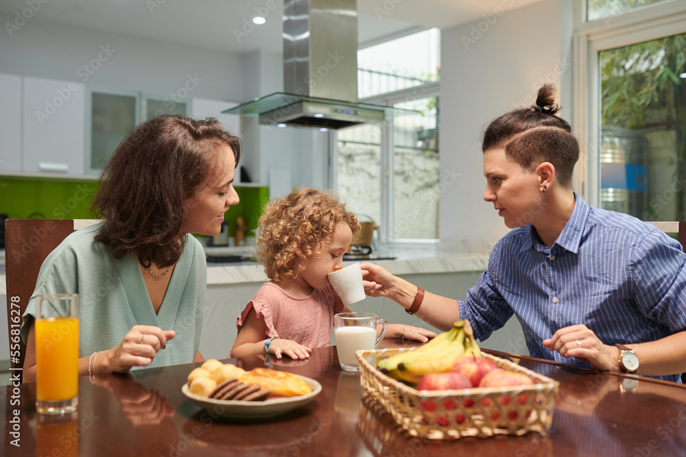 Lesbian couple with little daughter eating breakfast at kitchen table