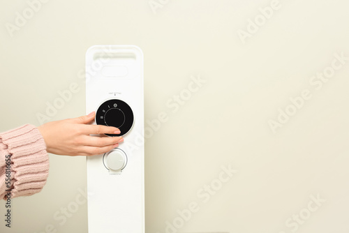 Young woman adjusting temperature on modern electric heater near beige wall, closeup. Space for text