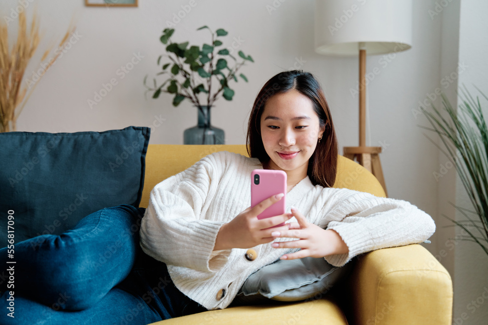 Young female in casual clothes sitting on sofa and browsing mobile phone while resting in cozy living room at home Young female in casual clothes sitting on sofa and browsing mobile phone while resting in cozy living room at home