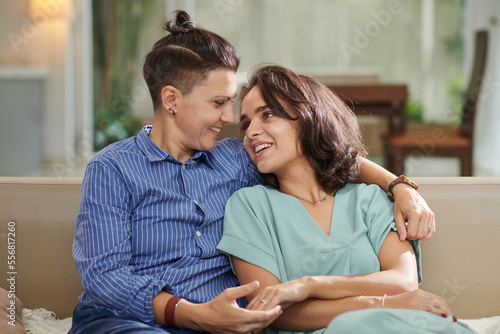 Portrait of married lesbian couple sitting on sofa at home and looking at each other