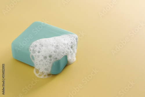 Soap bar with fluffy foam on yellow background, space for text