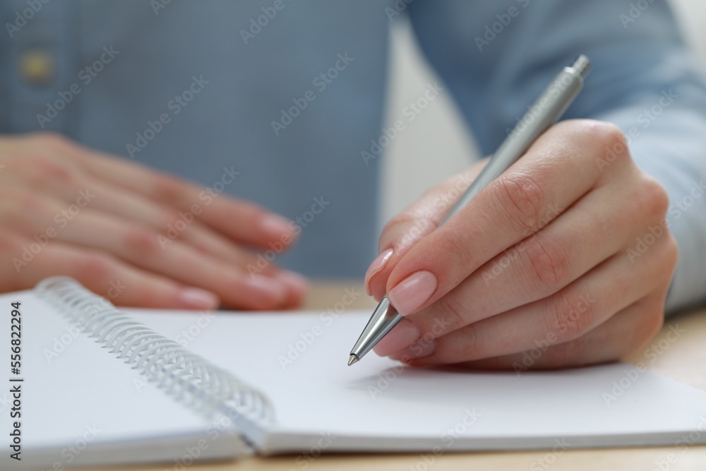 Woman writing with pen in notebook at wooden table, closeup Woman writing with pen in notebook at wooden table, closeup