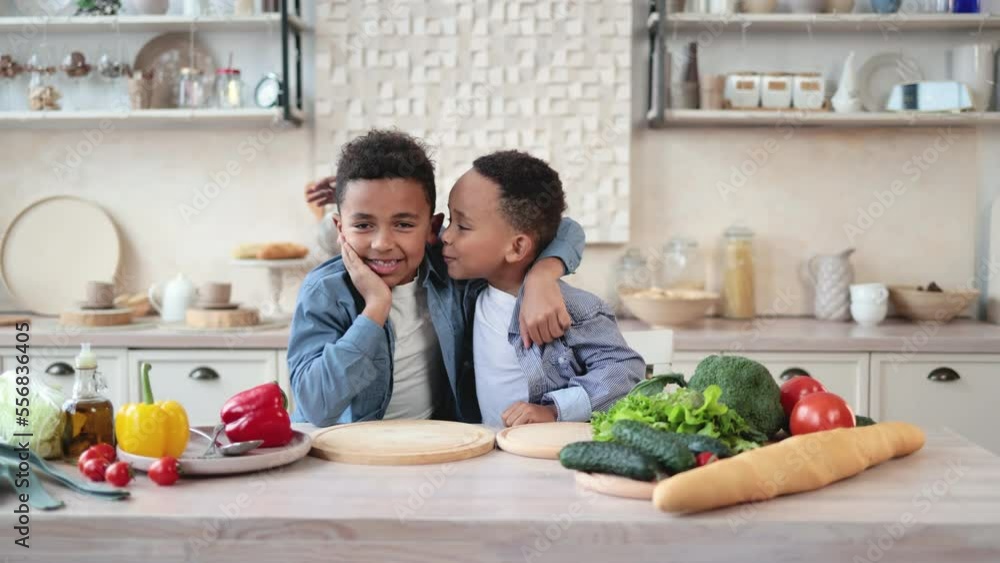 Smiling little cute african brothers boys in casual clothes sitting at table while touching cheeks satisfied of cooking salad. Beautiful african american children preparing healthy food on kitchen. Smiling little cute african brothers boys in casual clothes sitting at table while touching cheeks satisfied of cooking salad. Beautiful african american children preparing healthy food on kitchen.