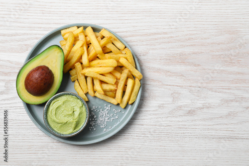 Plate with french fries, guacamole dip and avocado served on white wooden table, top view. Space for text