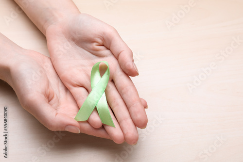 World Mental Health Day. Woman holding green ribbon on wooden background, top view with space for text