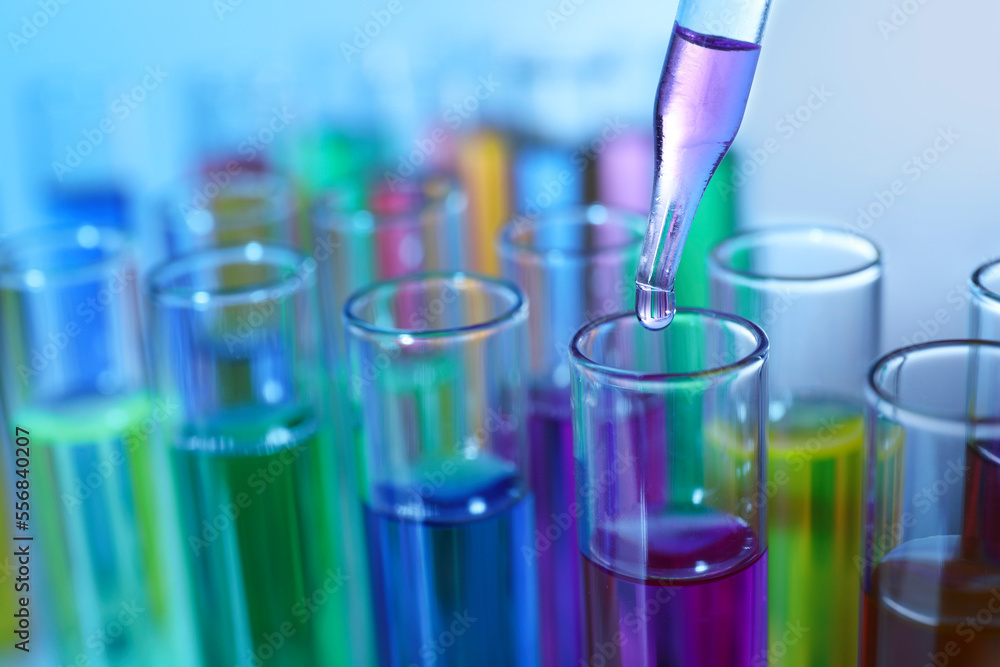 Dripping liquid from pipette into test tube on blurred background, closeup Dripping liquid from pipette into test tube on blurred background, closeup