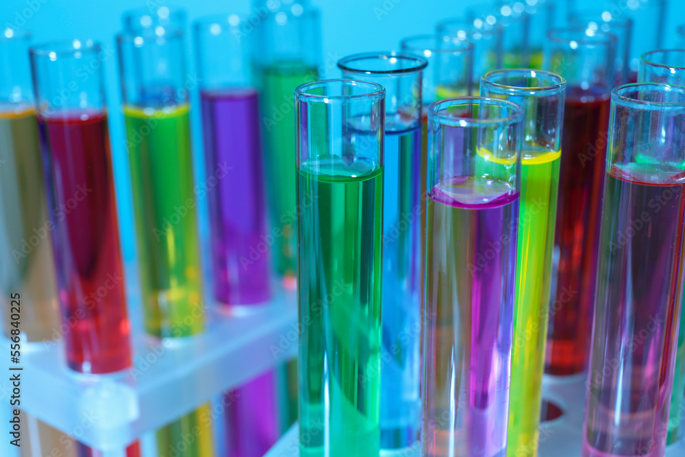 Many test tubes with colorful liquids on light blue background, closeup Many test tubes with colorful liquids on light blue background, closeup