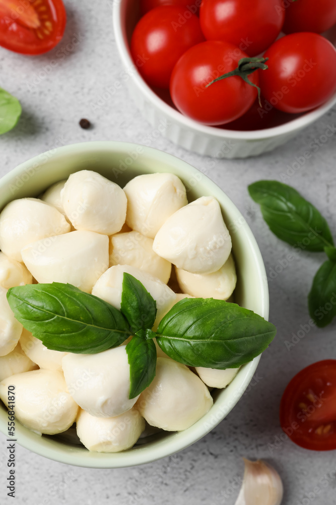 Delicious mozzarella balls in bowl, tomatoes and basil leaves on light gray table, flat lay Delicious mozzarella balls in bowl, tomatoes and basil leaves on light gray table, flat lay