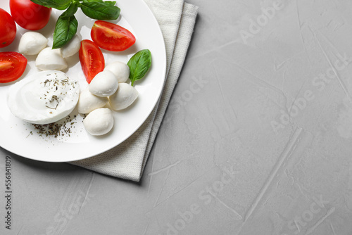 Delicious mozzarella with tomatoes and basil leaves on light gray table, top view. Space for text