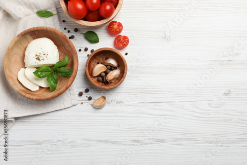 Delicious mozzarella with tomatoes and basil leaves on white wooden table  flat lay. Space for text