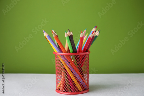 Many colorful pencils in holder on light table against green background