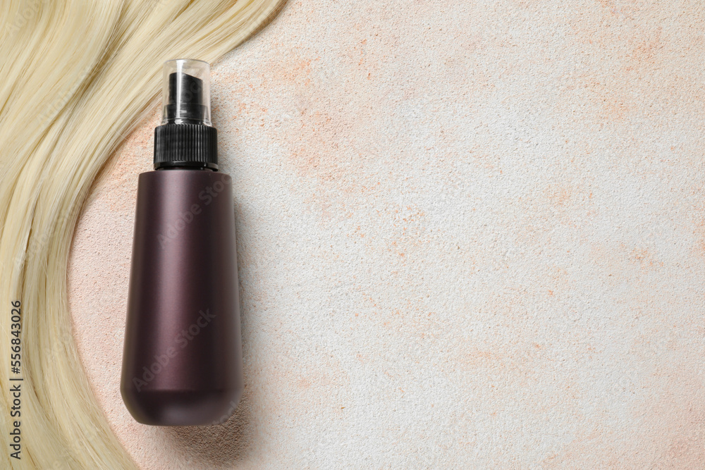 Spray bottle with thermal protection and lock of blonde hair on beige textured table, flat lay. Space for text