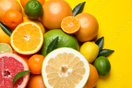 Different ripe citrus fruits with green leaves on yellow background, flat lay