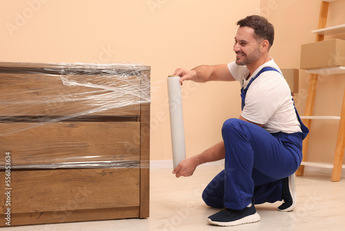 Workers wrapping chest of drawers in stretch film indoors