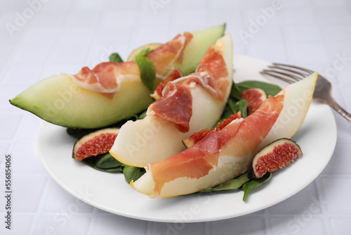 Tasty melon, jamon and figs on white tiled table, closeup