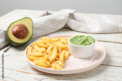 Plate with french fries, avocado and guacamole dip on white wooden table