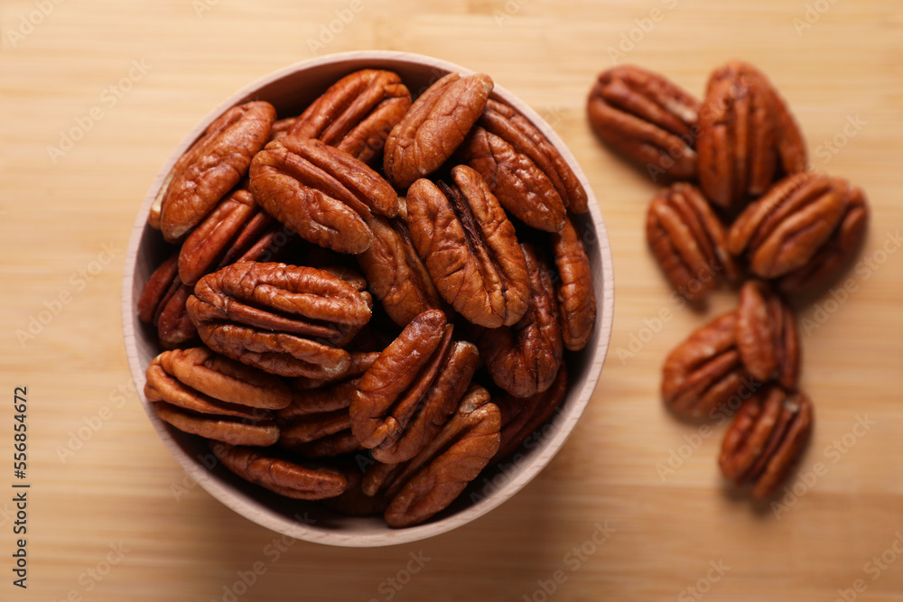 Tasty pecan nuts with bowl on wooden table, flat lay Tasty pecan nuts with bowl on wooden table, flat lay