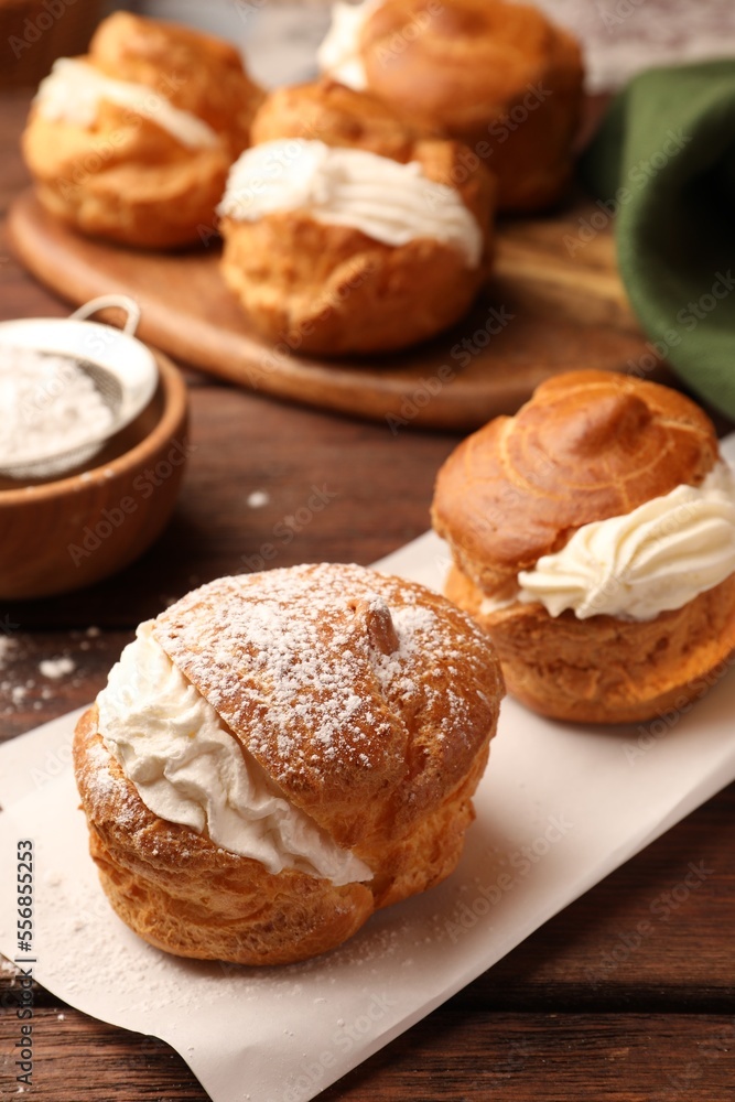 Delicious profiteroles with cream filling and powdered sugar on wooden table, closeup
