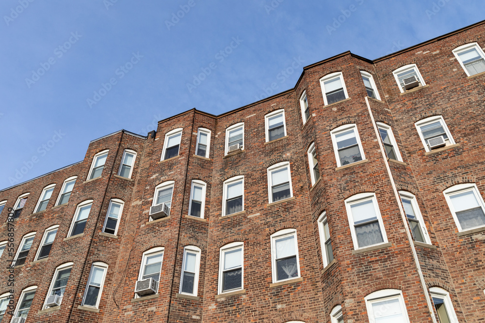 Oblique view of the undulating surface of a generic urban brick apartment building, view looking up at blue sky beyond, horizontal aspect