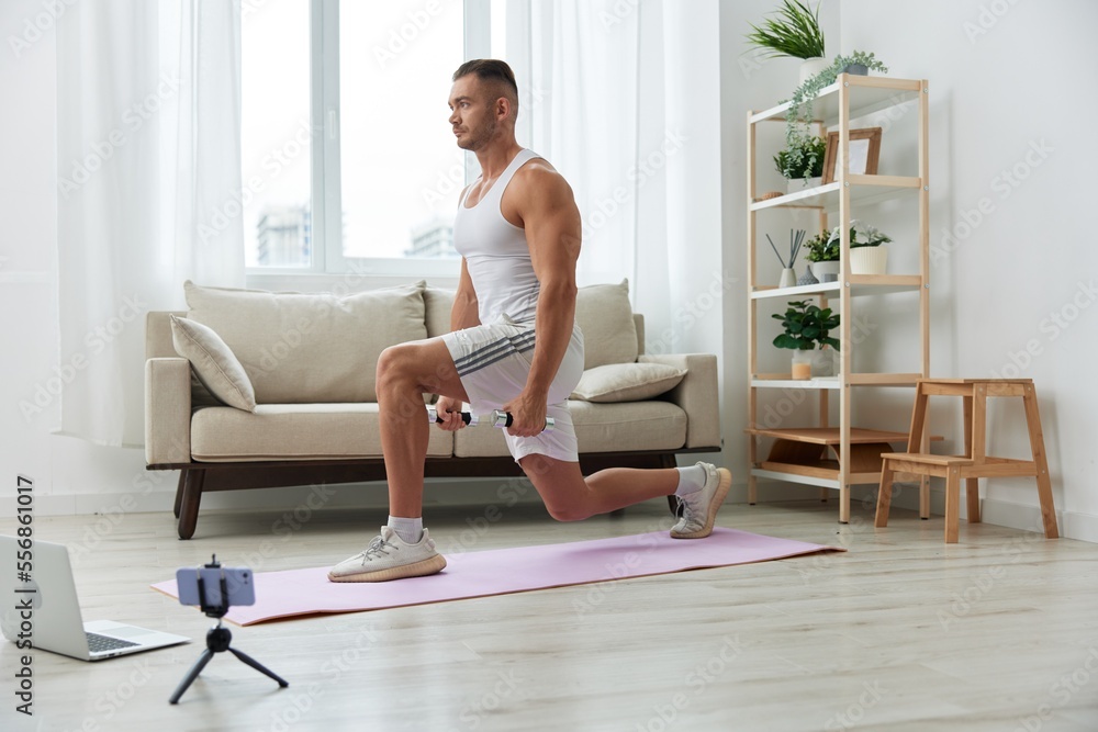 Man sports, watching a workout tape on his phone and repeating exercises sports blogger with dumbbells, pumped up man fitness trainer works out at home, the concept of health and body beauty Man sports, watching a workout tape on his phone and repeating exercises sports blogger with dumbbells, pumped up man fitness trainer works out at home, the concept of health and body beauty