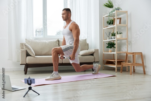 Man sports, watching a workout tape on his phone and repeating exercises sports blogger with dumbbells, pumped up man fitness trainer works out at home, the concept of health and body beauty