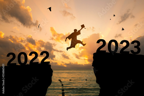 Silhouette Young man Graduation jumping on a cliff in 2023 over a sea cliff at sunset.education congratulation concept, Freedom and Happy new year, success in the future goal, and passing time.