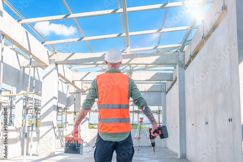 Male engineer wearing safety suit and hard hat holding toolbox and electric drill in construction site for building site survey in civil engineering project.