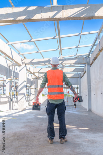 Male engineer wearing safety suit and hard hat holding toolbox and electric drill in construction site for building site survey in civil engineering project.