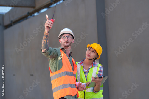 Two professionals inspect construction site of commercial building, industrial building, real estate project  civil engineer, investor using laplet in background crane, skyscraper, concrete formwork