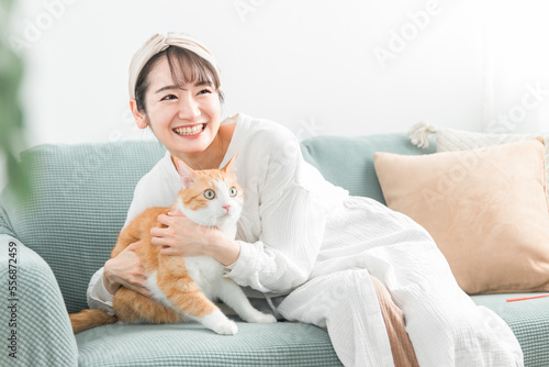 家のソファで猫を抱っこする飼い主のアジア人女性
