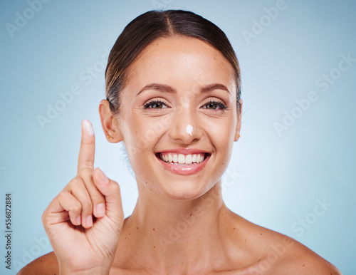 Portrait, beauty and skincare with a model woman posing in studio on a blue background with lotion on her finger. Face, skin or moisturizer with an attractive young female posing to promote a product