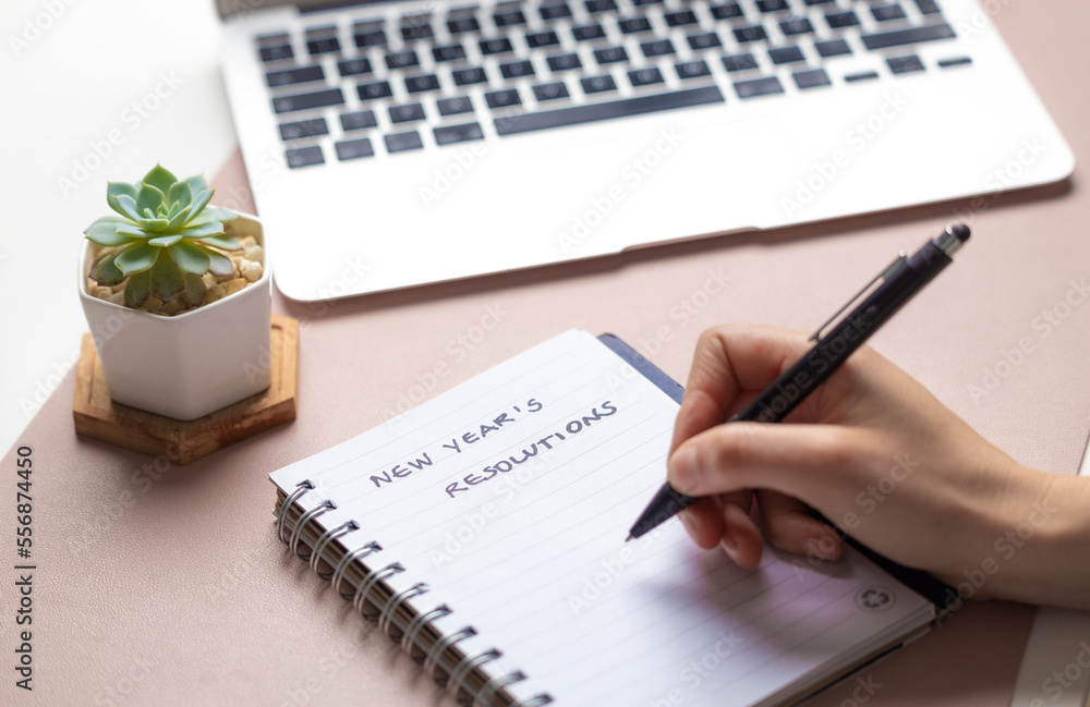woman writing new year's resolutions with a black pen on a notebook over a  desk with a computer and a plant Stock-Foto | Adobe Stock