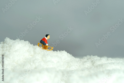 Miniature people toy figure photography. Winter holiday. A boy riding wooden sledge, sledding down the hill