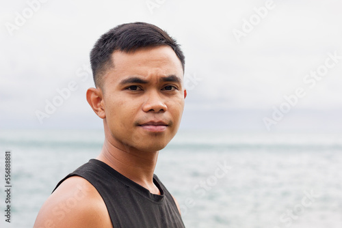 Serious portrait of young Filipino man by the sea on cloudy day. Asian male model concept