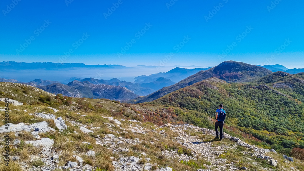 Man with backpack and hat on top of Goli Vrh with scenic view on mountain chains of Dinaric Alps and Lake Skadar National Park, Montenegro, Balkan, Europe. Valley covered by mystical fog. Freedom