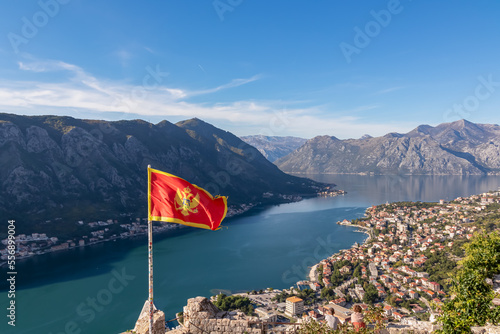 Montenegro flag blowing in wind with scenic view from St Ivan fortress on Kotor bay in sunny summer, Adriatic Mediterranean Sea, Montenegro, Balkan Peninsula, Europe. Fjord winding along coastal towns photo