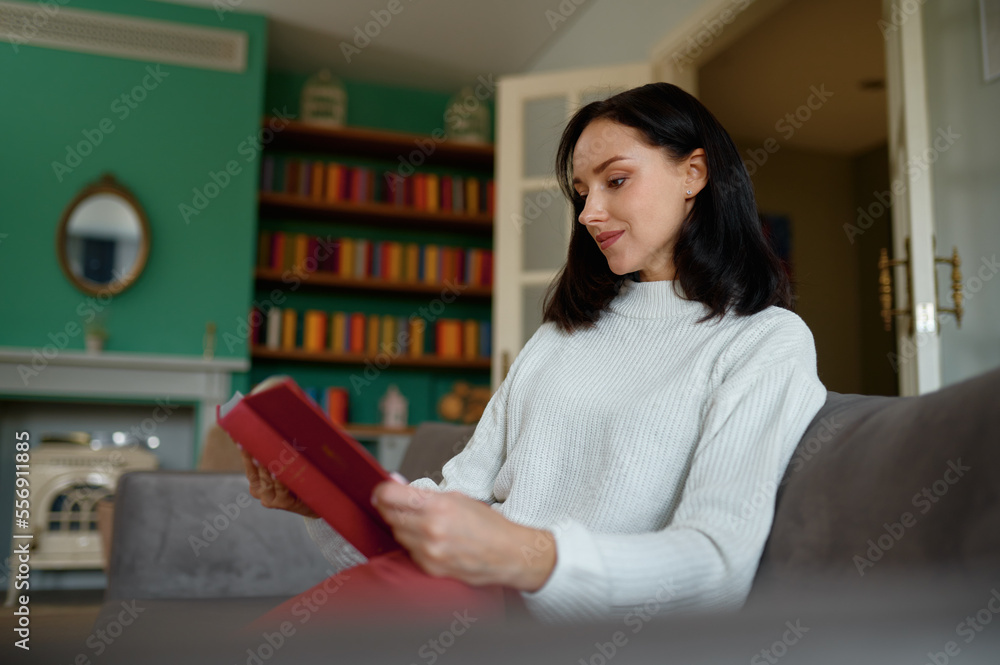 Millennial woman reading book sitting in cozy sofa at home Millennial woman reading book sitting in cozy sofa at home