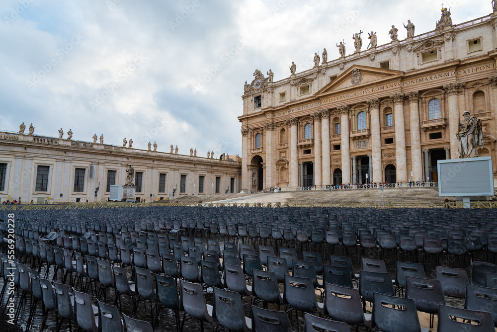 Naklejka premium Empty seats in front of the facade of the famous Saint Peter Basilica, in Vatican city, Rome, Italy. Overcasted sky on the background.