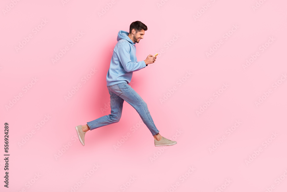 Full length profile side photo of glad man addicted user hold telephone writing typing friend empty space isolated on pink color background