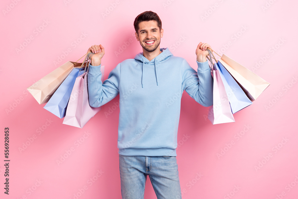 Photo of pretty excited guy dressed blue sweatshirt smiling rising shoppers isolated pink color background Photo of pretty excited guy dressed blue sweatshirt smiling rising shoppers isolated pink color background