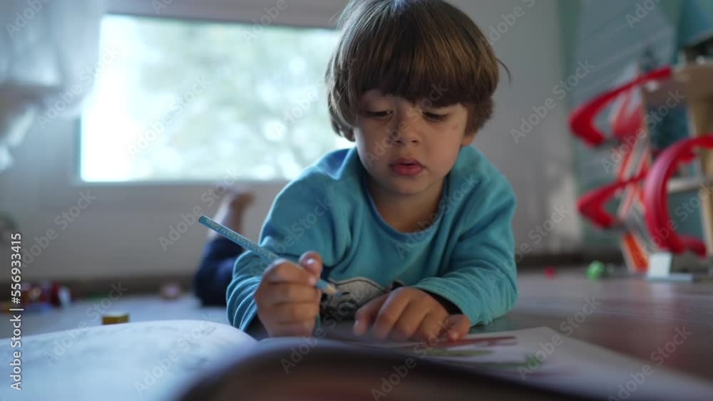 One Concentrated child doing school homework activity in bedroom wearing pajamas. Kid laying on floor holding color pencil One Concentrated child doing school homework activity in bedroom wearing pajamas. Kid laying on floor holding color pencil